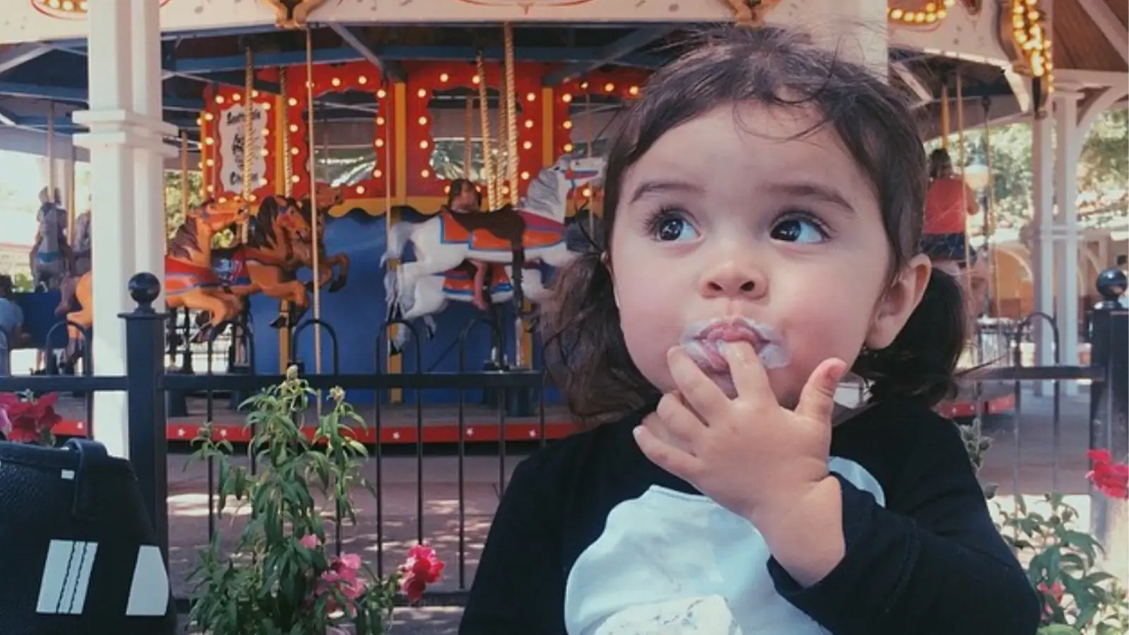 Young child sitting in front of a carousel enjoying her ice cream.