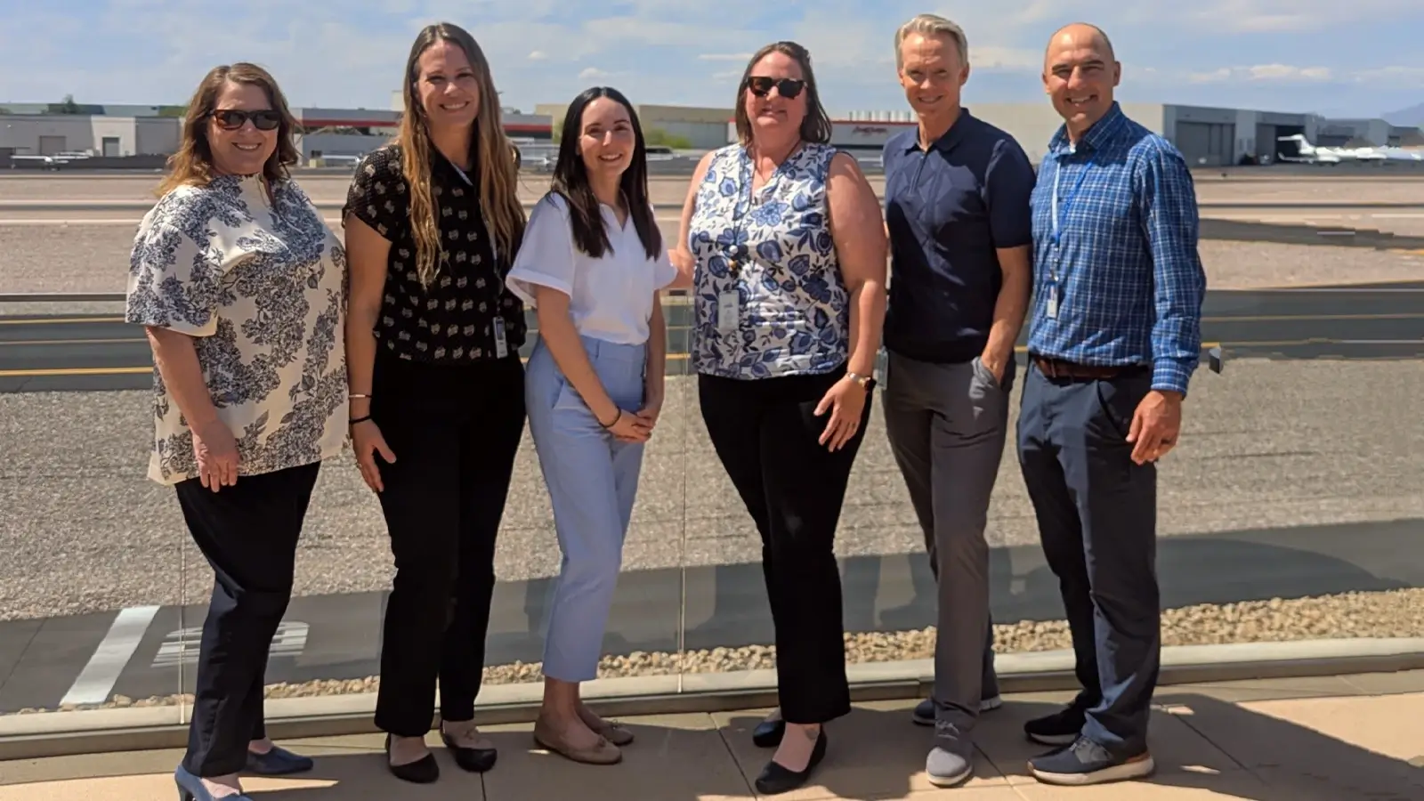 Six Scottsdale team members stand smiling outside on the tarmac near several airplanes. Scottsdale's business services assist in workforce development and site selection.