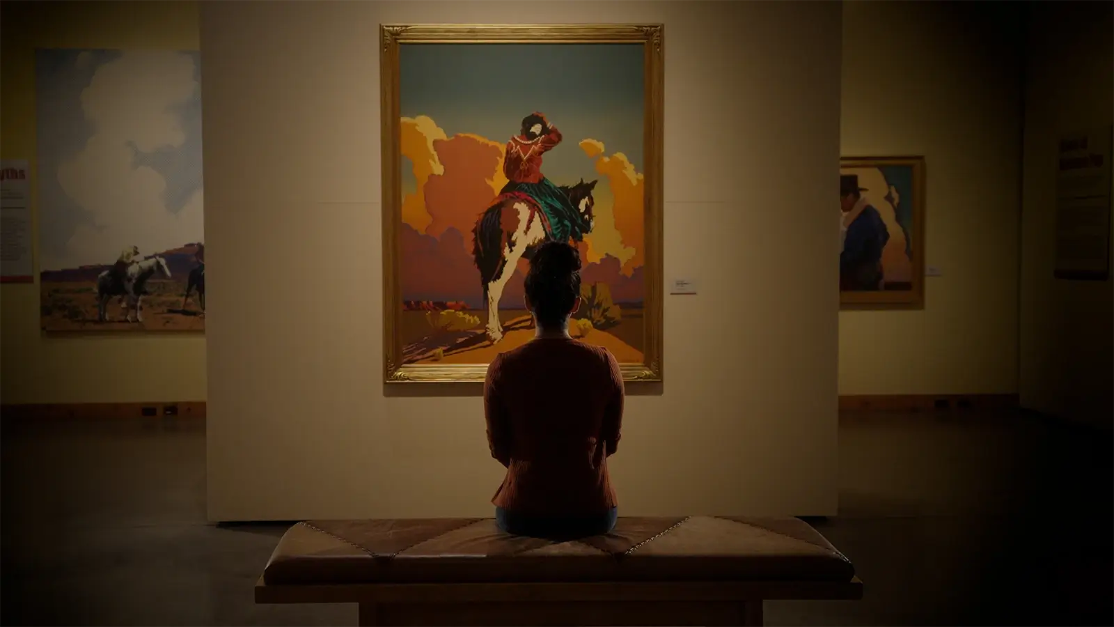 Art gallery patron sitting on a bench viewing an art piece.