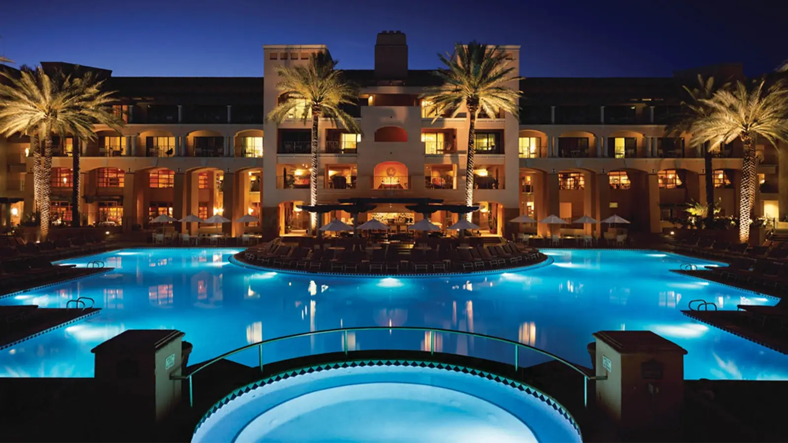 Nighttime photo of blue lit pool with the resort in the background.