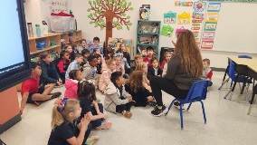 Teacher reading a book to children sitting around her on the floor.