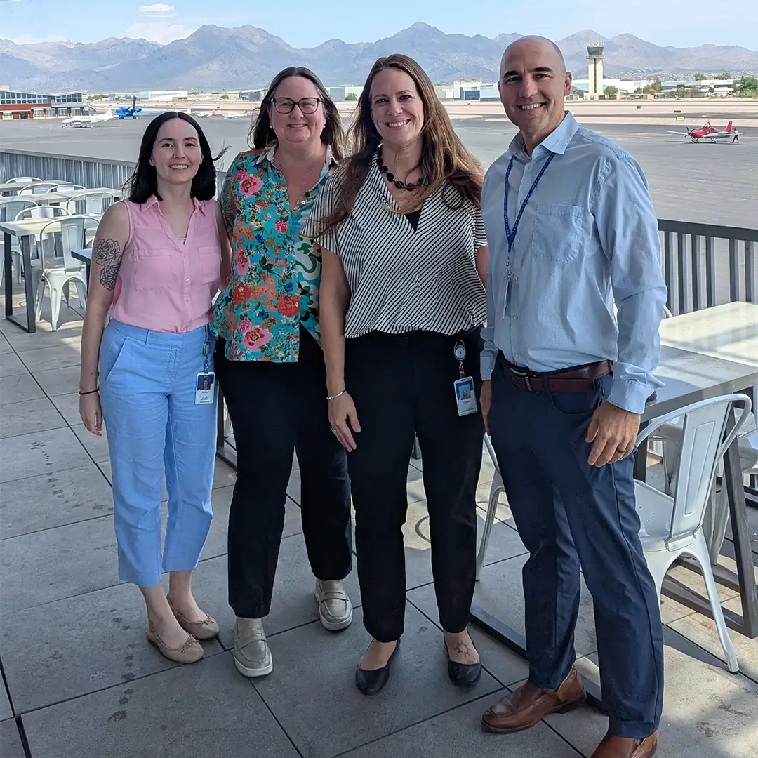 Choose Scottsdale staff pose in front of a large red "LOVE" sculpture. The team wears matching shirts and sunglasses, creating a cohesive look.